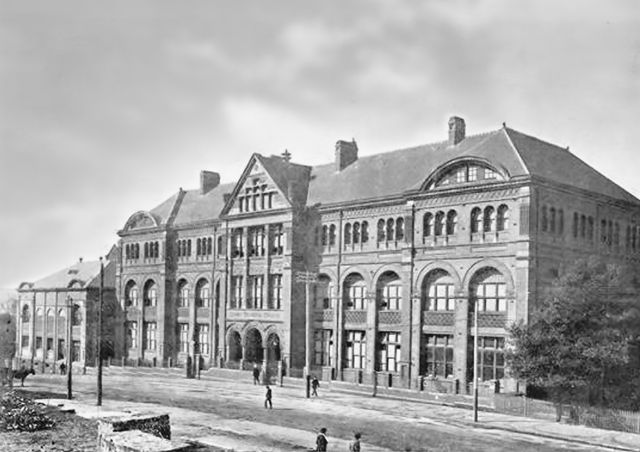 A black-and-white archival photo of an historic building with arched windows and a large entrance. The architecture is grand, with ornate details along the façade.