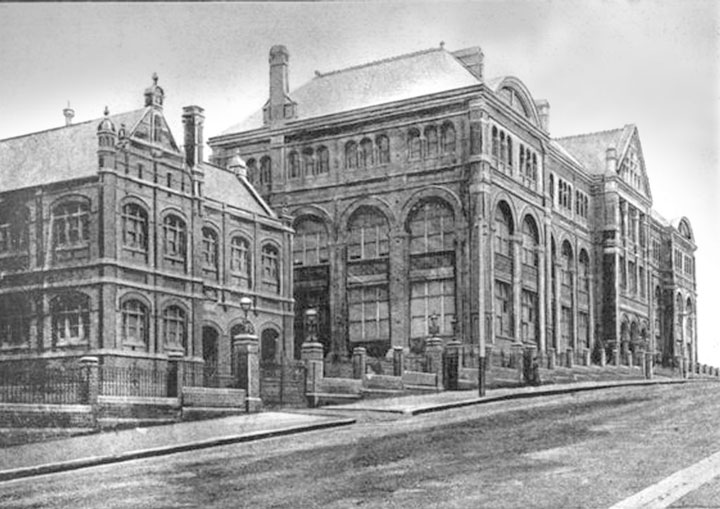 Historic building with arched windows on a sloped street, featuring stone details and vintage fencing.