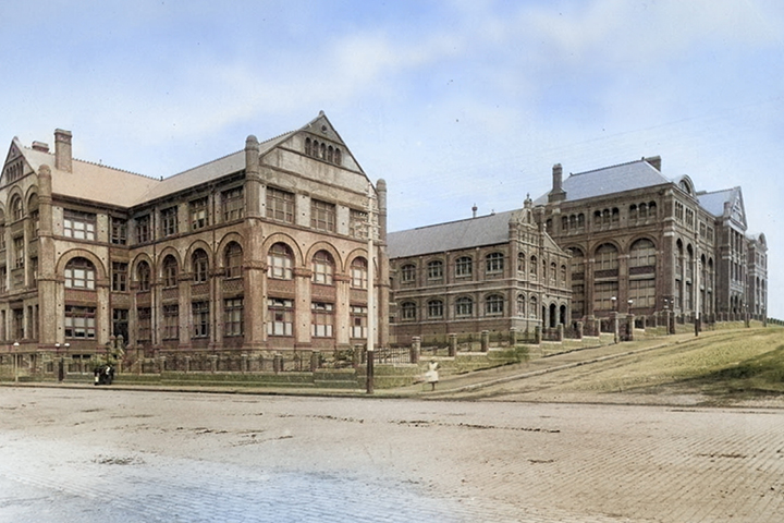 Historical buildings made of brick and sandstone, with a neat hedge around the border of the block. Image is an old photograph.