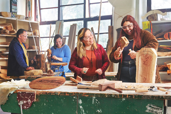 A female Aboriginal teacher patiently guides a young student as they work on their sculpture project.