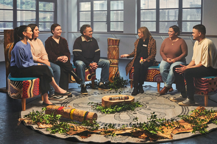 A group of Indigenous Australians sitting in a circle, engaged in a Yarning session inside a modern building.