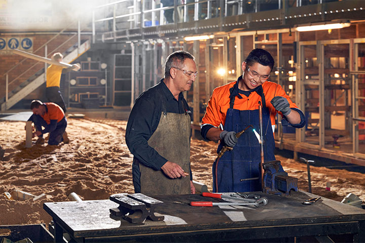 Teacher and student working together on a construction site, welding a pipe.