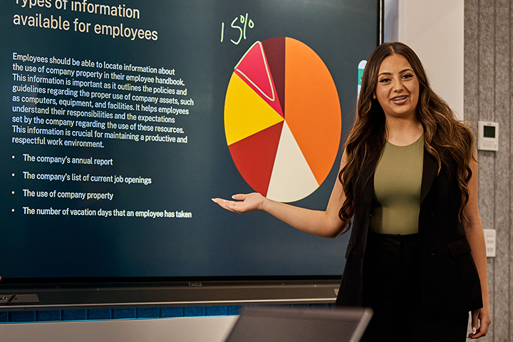 A business student confidently presents to her classmates and teacher.