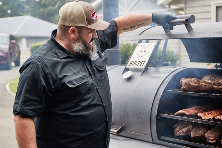 BBQ pitmaster tending to a large smoker called the Hogpit