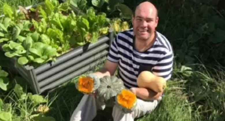 A photo of Andrew Radford sitting amongst plants, holding pumpkins. 
