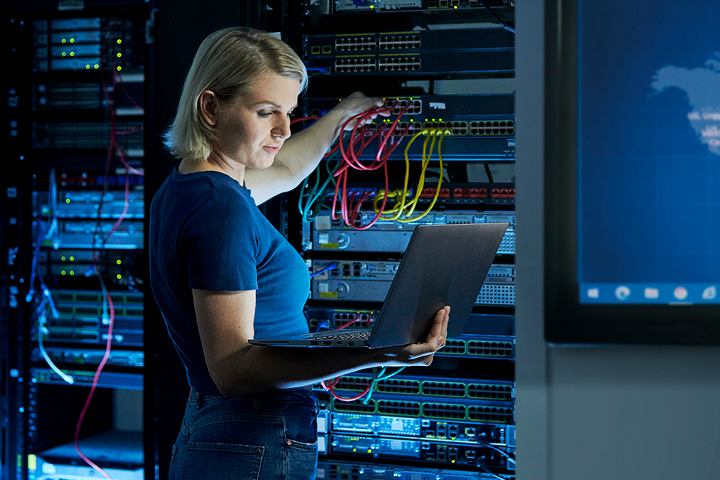 Female network engineer working on a server and holding a laptop