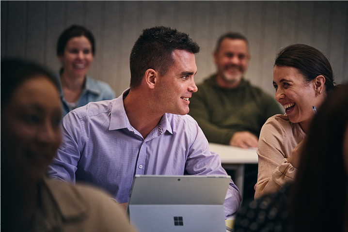 A student with his laptop open engages with a laughing fellow student in a face-to-face class. 