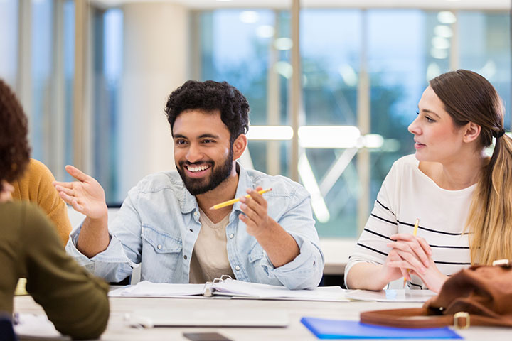 Cheerful student animatedly conversing with peers on campus, smiling and using hand gestures to emphasise points.