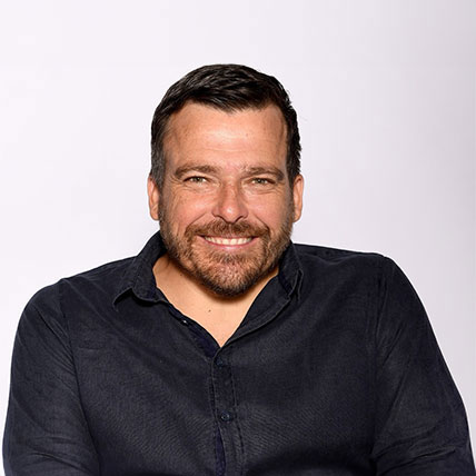 The image shows Kurt Fearnley in a black collared shirt. He has short brown hair and is smiling.