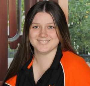 A headshot of Netteisha Gibson, smiling at the camera. She has long straight brown hair and is wearing a black and orange polo top.