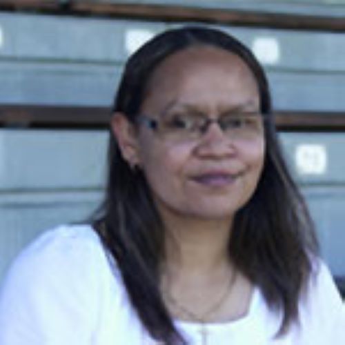 A headshot image of Rhonda Sampson smiling at the camera. She is wearing a white shirt. She has long dark hair and glasses. 