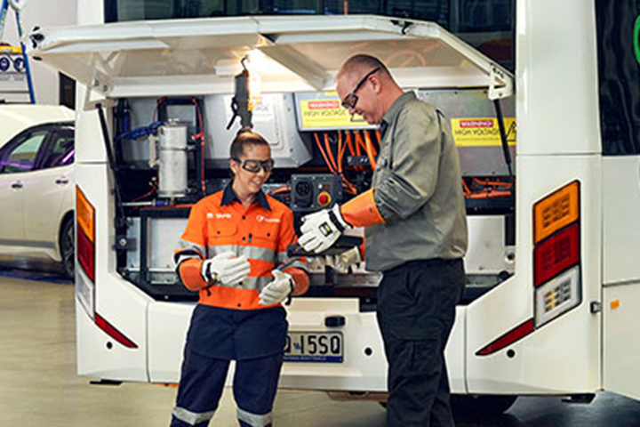 A young female mechanic with her teacher inspecting an EV bus.