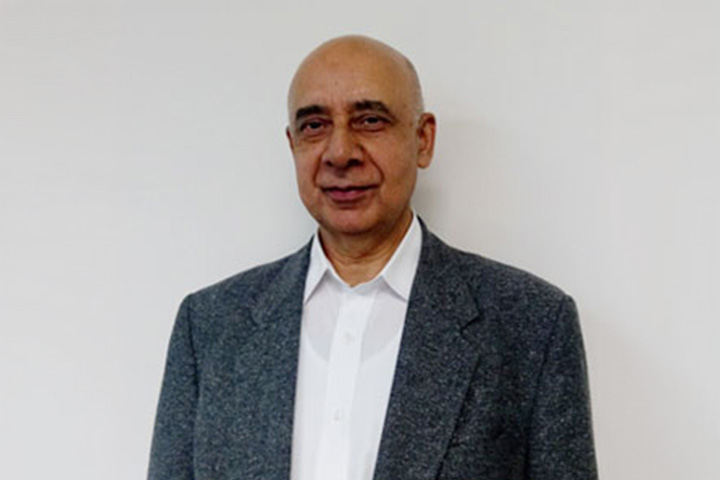 Dr. Amir Christi, Head Teacher of Information Technology at TAFE NSW, smiles knowingly at the camera. He is sharply dressed in a crisp white shirt and a charcoal tweed blazer with notched lapels.