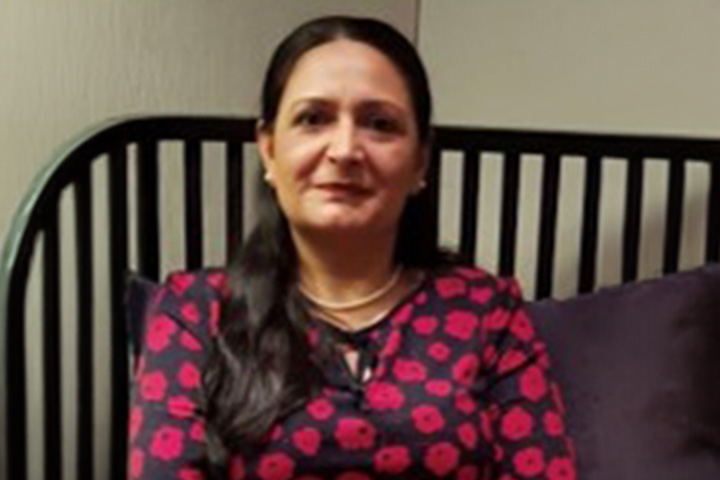 TAFE NSW Castle Hill campus Nursing teacher Paramjeet Kaur is seated on a cushioned bench, wearing a black dress adorned with vibrant red poppies.