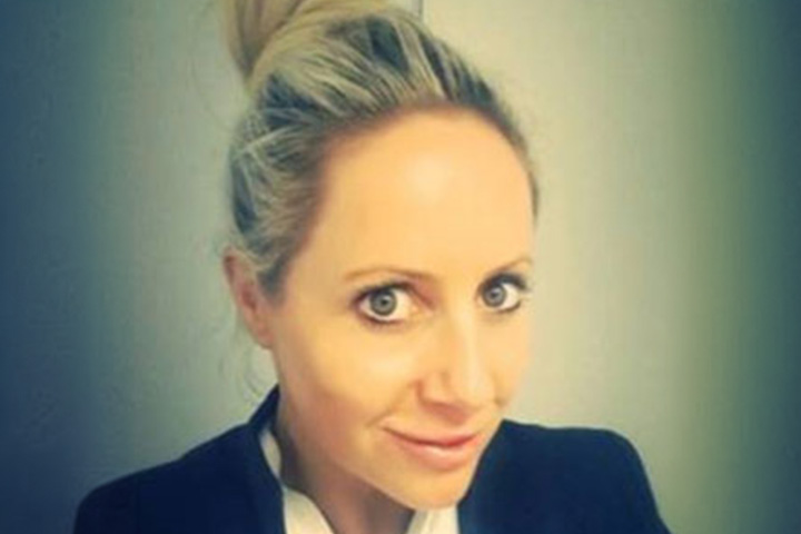 TAFE NSW Ultimo campus Beauty and Makeup teacher Trina Storey-Hollis is dressed in a polished white shirt and a classic black blazer. Her blonde hair is styled in an elegant top knot bun.