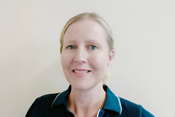 Wendy Millis, Allied Health and Fitness teacher at TAFE NSW Port Macquarie campus, smiles directly at the camera while wearing a dark green polo shirt. She stands in front of a wall.
