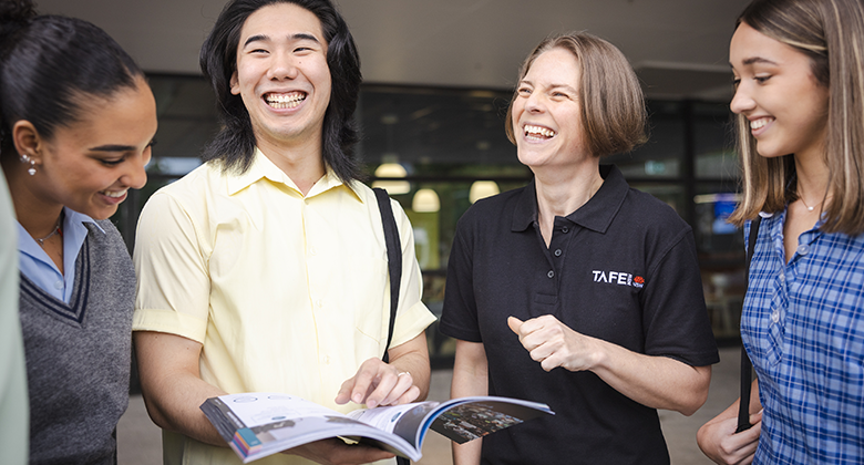 Students are gathered together with a TAFE NSW staff member. They are smiling and laughing while looking at a brochure that shows the range of courses that are available to them in their final years, or after high school.