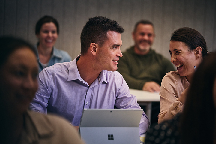 A student with his laptop open engaging with a smiling fellow student in a face-to-face class.