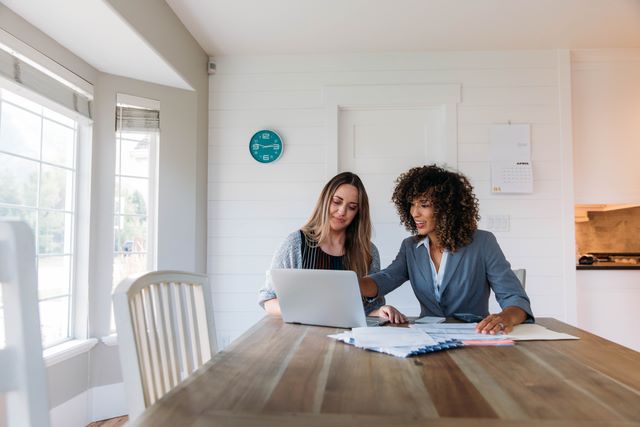 Two women working together at a table with a laptop and documents