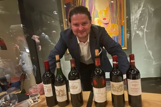 Daniel Airoldi smiles to the camera with a selection of Airoldi fine wines displayed on a table before him.