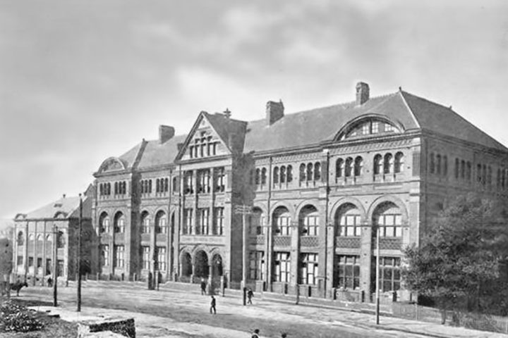 A black-and-white archival photo of an historic building with arched windows and a large entrance. The architecture is grand, with ornate details along the façade.