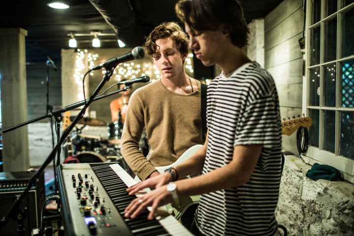 Two young men are playing music together. One is playing keyboards and one is on the guitar. They both have microphones set up.