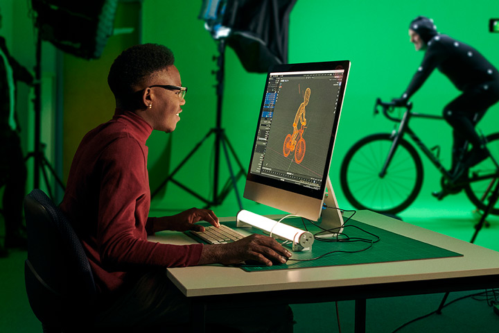 A student works on an animation project at a computer, surrounded by sketches and digital tools.