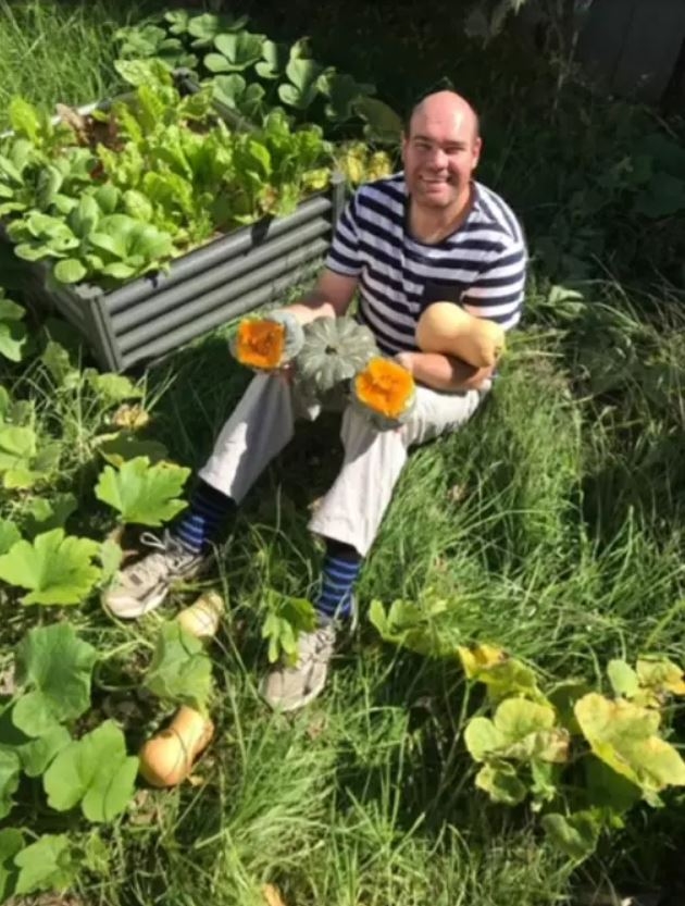 A photo of Andrew Radford sitting amongst plants, holding pumpkins. 