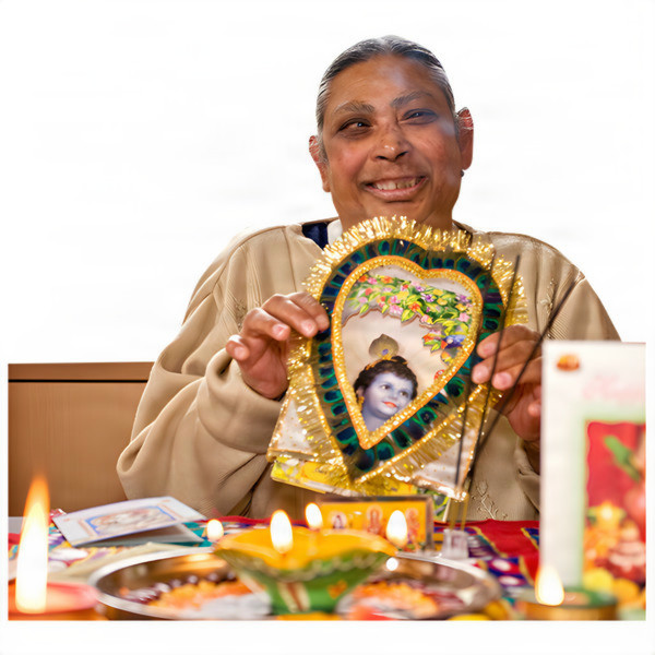 Elderly person holding a decorative framed image of a deity at a table with lit candles and offerings.
