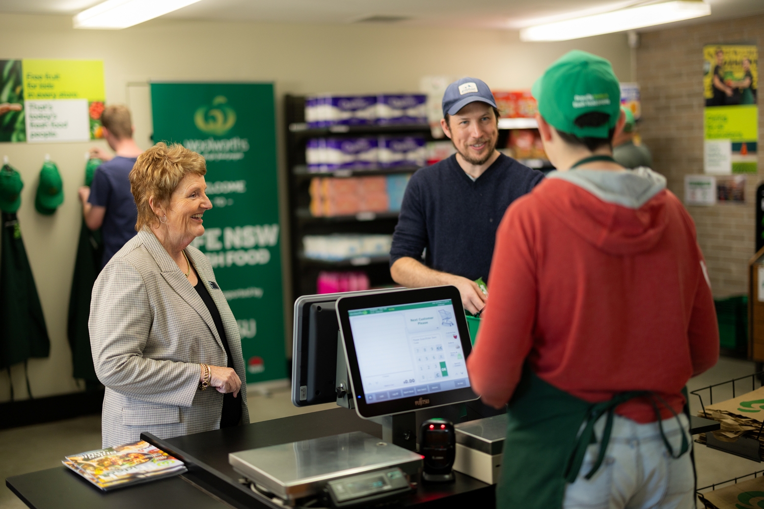 A student serving a customer at a practise supermarket counter with 2 people.