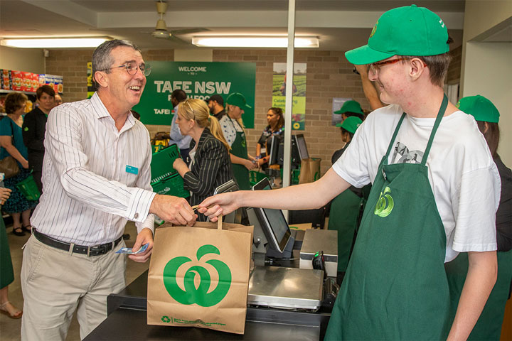 A customer is handed groceries at a TAFE NSW supermarket checkout.