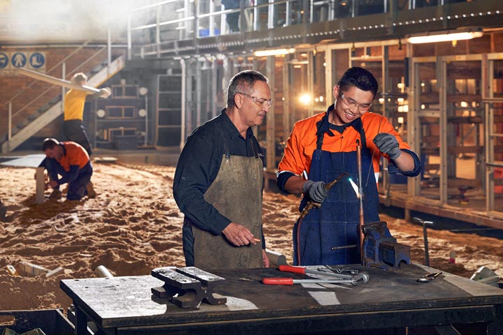 Teacher and student working together on a construction site, skillfully welding a pipe to enhance practical knowledge in the field of construction and welding.