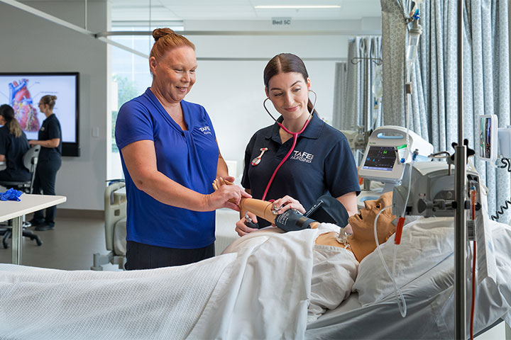 Nursing student and teacher practicing bedside manner with a realistic mannequin, honing essential skills for patient care and communication.