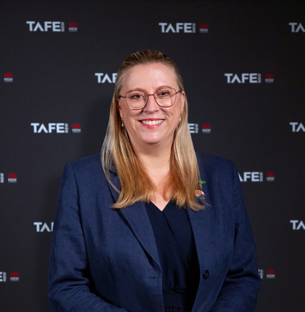 The image shows Chloe Read in a dark blue blazer standing in front of a TAFE NSW black backdrop. She has long blonde hair and is wearing glasses.
