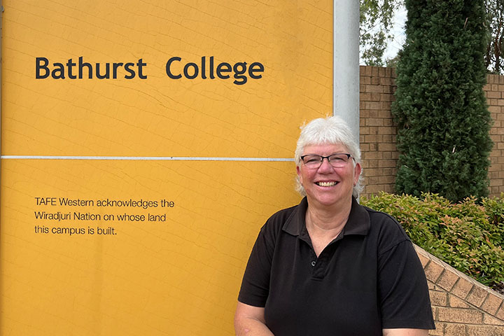 TAFE NSW Auslan Teacher Wendy Daley standing in front of Bathurst College stand