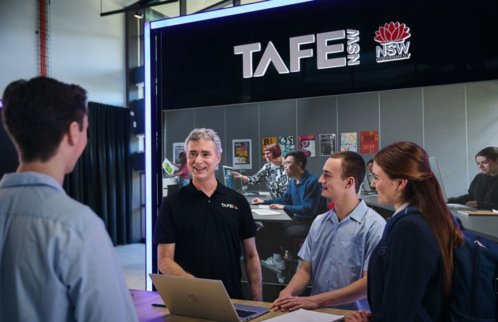 A TAFE NSW staff member stands talking to prospective students at a TAFE NSW expo stall.