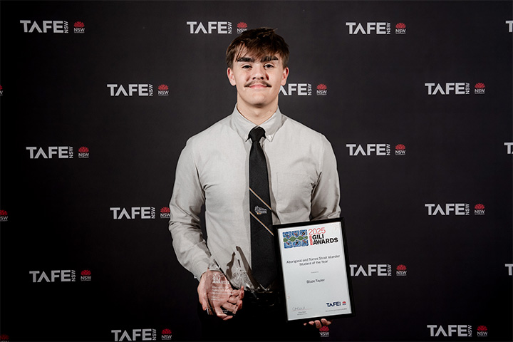 A person holding an award and a certificate at a TAFE NSW Gili Awards. The background features the TAFE NSW logo repeatedly.