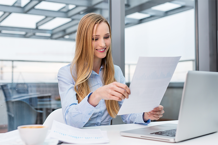 A lady sits at a desk in an office and looks at a form