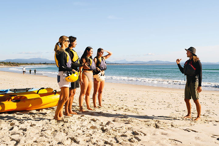 A group of young people listening to a surf instructor on a sunny Australian beach before entering the water.