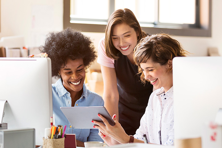 Three colleagues in a modern office collaborate around desks with computers and a tablet, discussing strategies for authentic brand alignment and business growth.