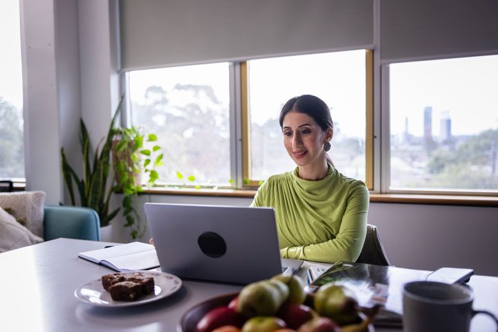 A woman working from home on a laptop, with a stunning city skyline view through the window.