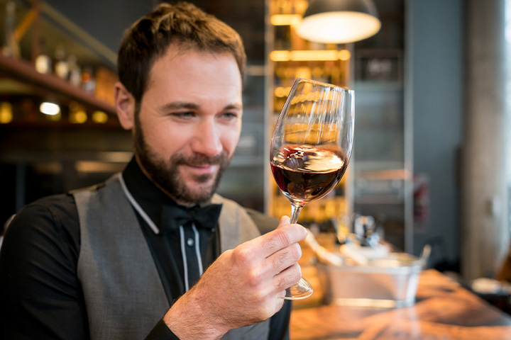 A male sommelier inspects a glass of red wine