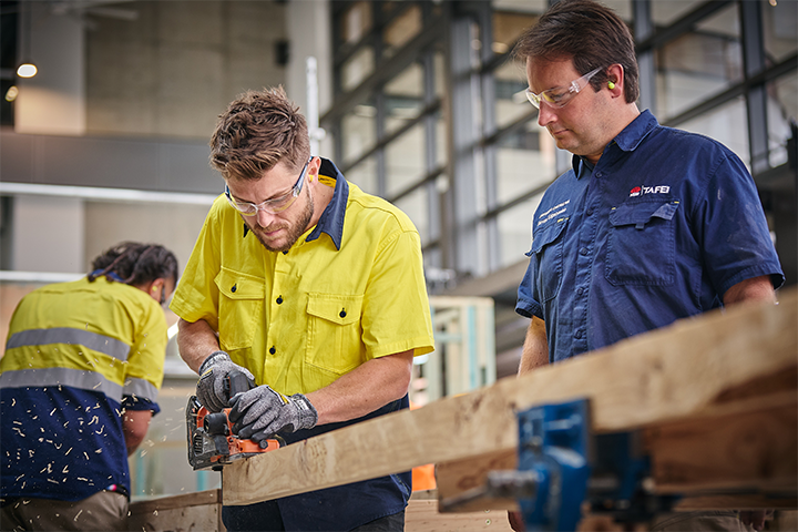 Carpentry student sawing wood with TAFE NSW teacher supervising
