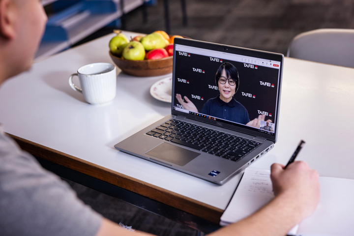 A student sits at their laptop, engaged in a video conference with a TAFE NSW teacher.